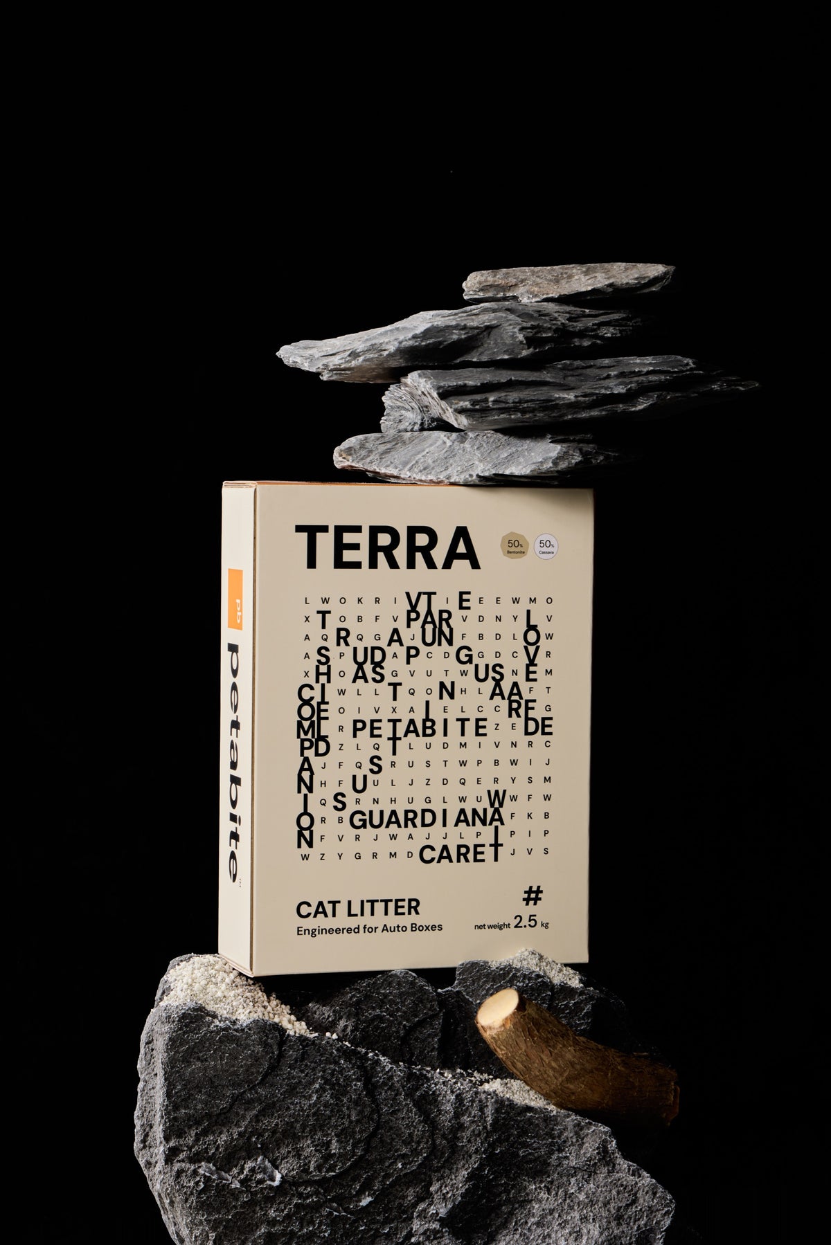 A Terra cat litter box among layered rocks with cassava root against a black studio background